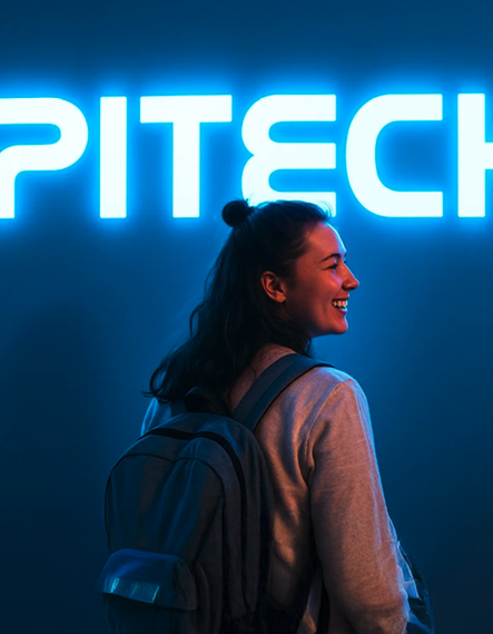 Estudiante de Epitech sonriendo bajo un rótulo luminoso de Epitech